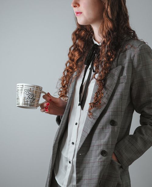 Free Businesswoman in plaid blazer holding a mug, gray background. Stock Photo