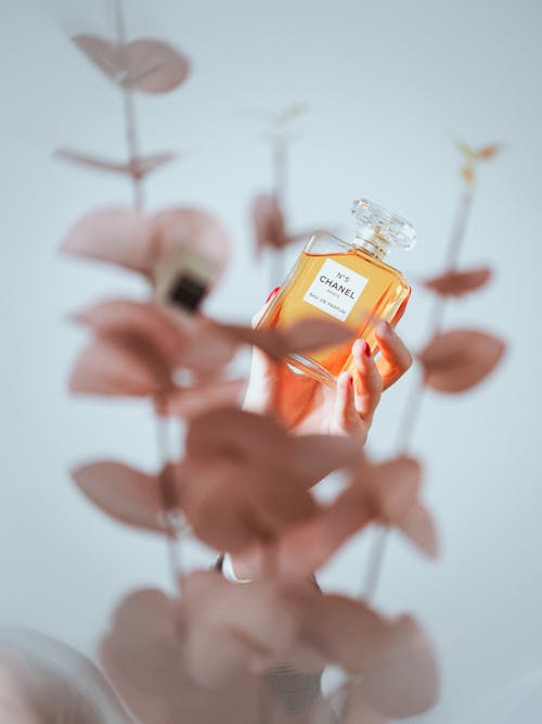 A person holding a bottle of perfume in front of some flowers