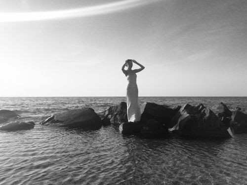 Free Elegant black and white photo of woman in dress standing on coastal rocks. Stock Photo