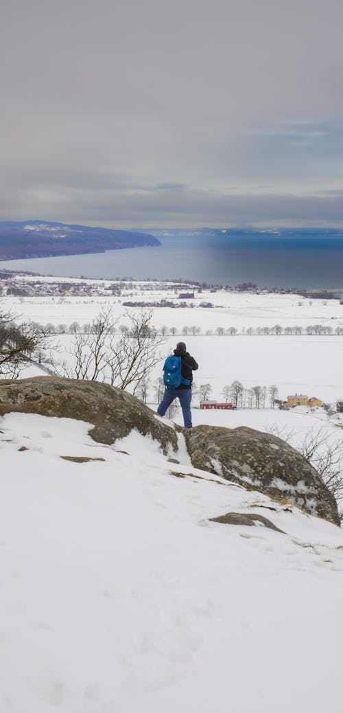 A person standing on top of a snowy hill looking out over the ocean