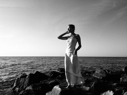 Free Black and white photo of a woman posing on seaside rocks in a long dress. Stock Photo