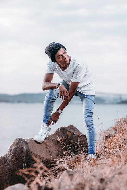 Free A stylish young man in casual attire poses on rocks by the sea on a cloudy day. Stock Photo