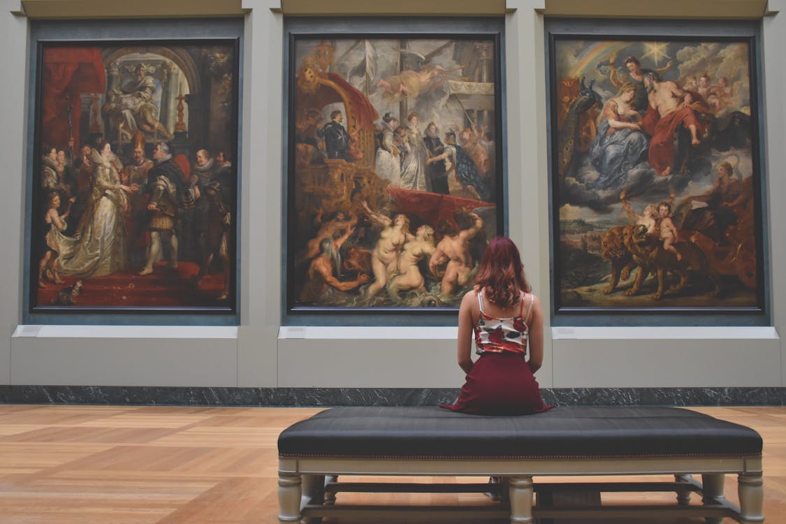 Free Woman Sitting on Ottoman in Front of Three Paintings Stock Photo