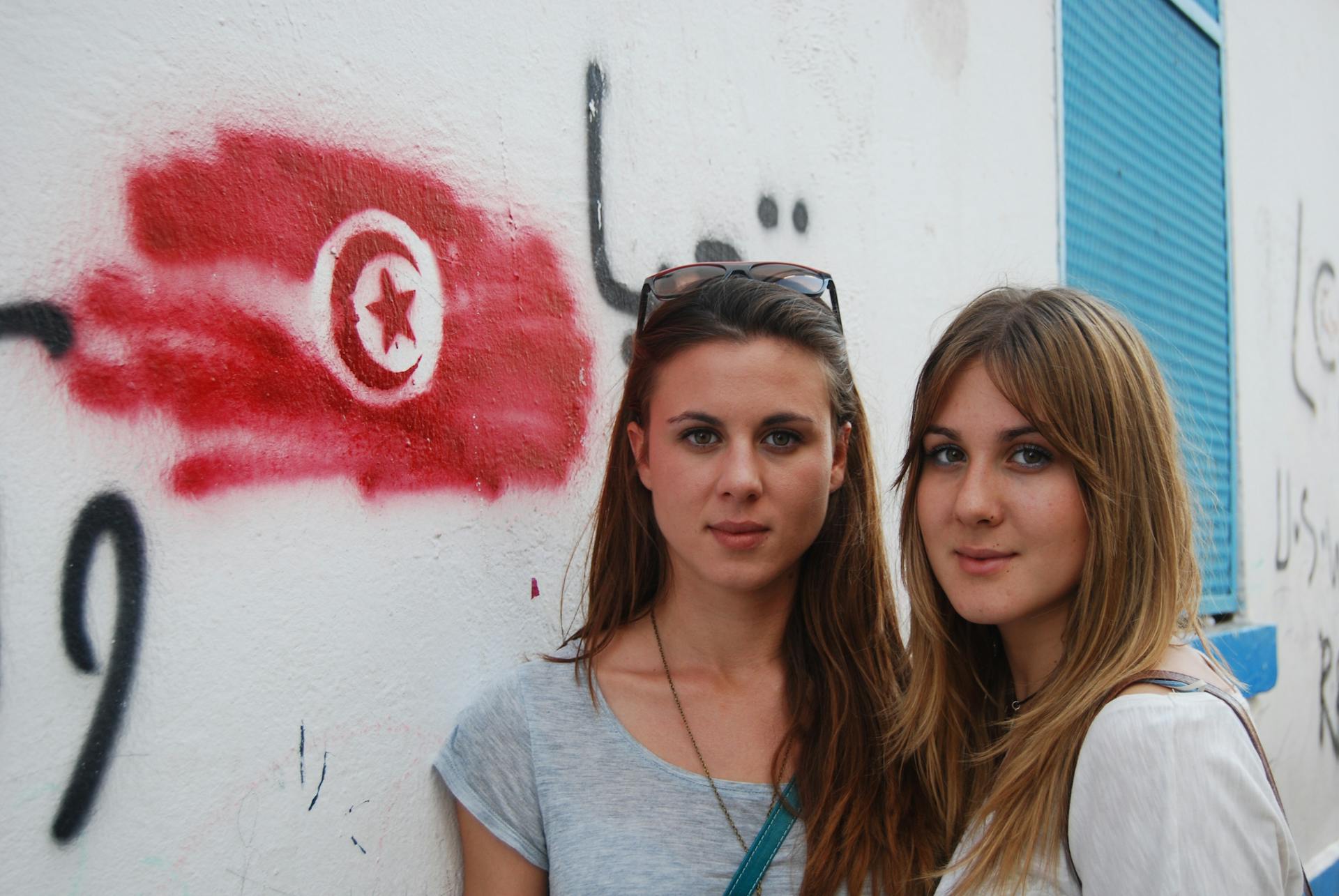 Two women pose in front of graffiti featuring the Tunisian flag in Tunis.