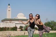 阳光明媚的一天，两名年轻女子在清真寺前快乐地摆着姿势