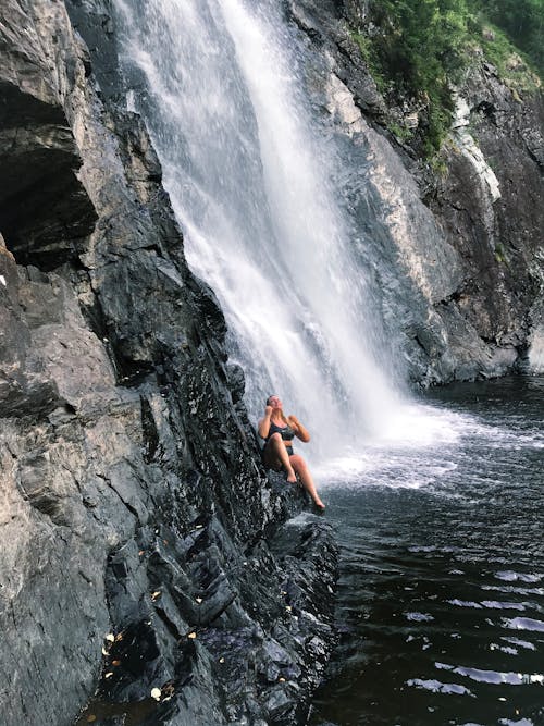 Человек, сидящий на скале возле водопада