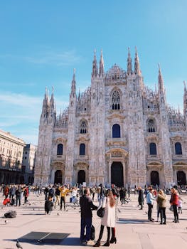 The stunning Milan Cathedral under bright skies, surrounded by a lively crowd in the bustling Piazza del Duomo. by julie aagaard