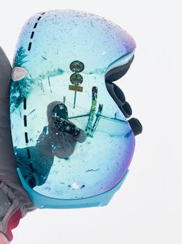 滑雪护目镜的特写镜头映出白雪皑皑的冬季风景，突显了寒冷天气与覆雪树木