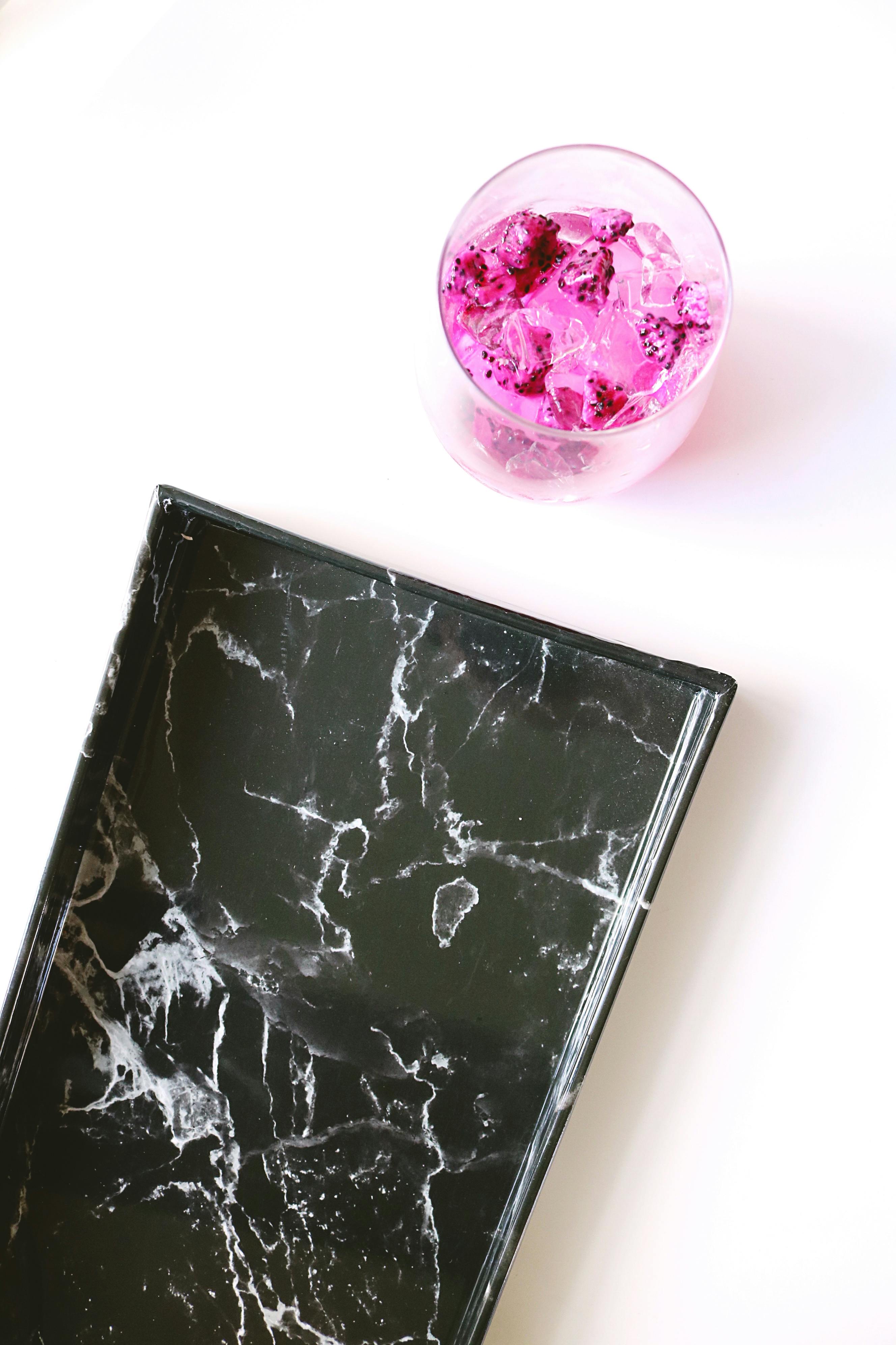 光滑的黑色大理石托盘上，放着充满活力的粉红色饮料和冰块