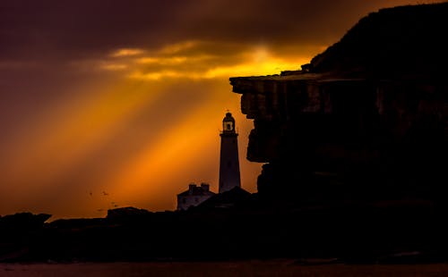 A lighthouse is silhouetted against the sun