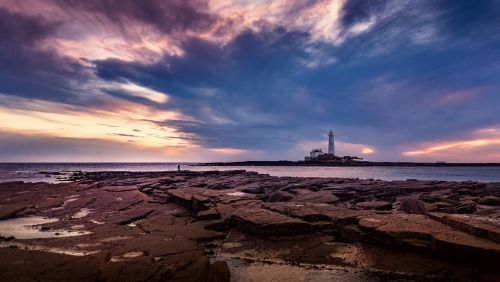 Free Breathtaking sunset with a lighthouse overlooking rocky ocean shore. Stock Photo
