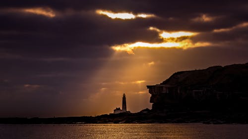 A lighthouse is silhouetted against the sun