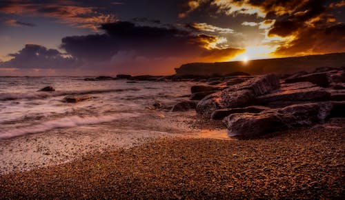 A sunset on the beach with rocks and water