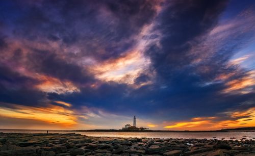 Free A stunning view of a lighthouse at sunset, with vibrant skies and rocky seascape. Stock Photo
