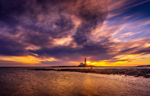 Free Beautiful ocean sunset scene with a lighthouse on the horizon. Stock Photo