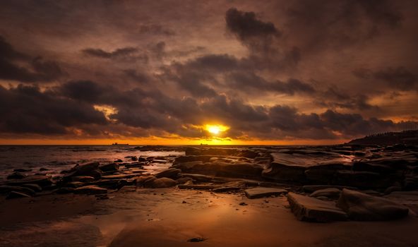 A breathtaking sunset over a rocky beach, capturing the dramatic beauty of the seascape.