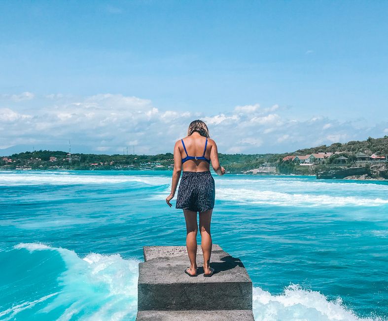 A woman stands on a pier, embracing the tropical ocean view in Bali, Indonesia. Perfect summer escape.