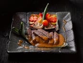 一盘深色餐盘中，优雅的牛肉菜肴搭配蔬菜与酱汁，宛如一件烹饪艺术品