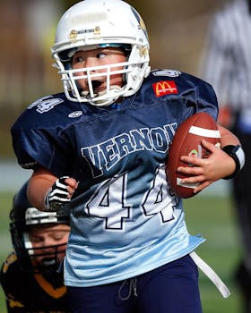 球场上，一个年轻的孩子穿着足球装备，手里拿着一个球