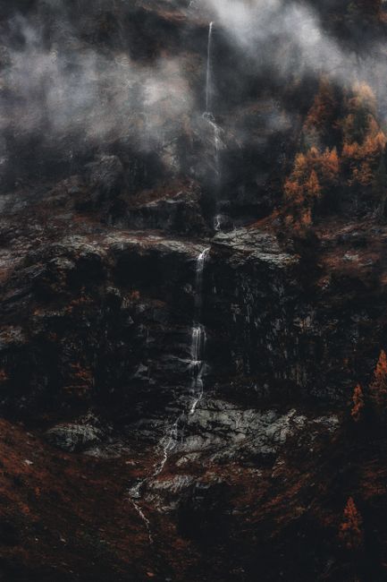 A serene waterfall cascades down rocky cliffs, enveloped in mist, creating a tranquil nature scene.
