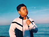 晴朗的天空下，一个穿着时尚夹克的小男孩自信地凝视着大海