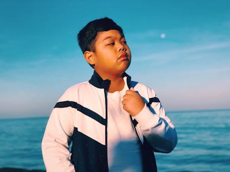 晴朗的天空下，一个穿着时尚夹克的小男孩自信地凝视着大海