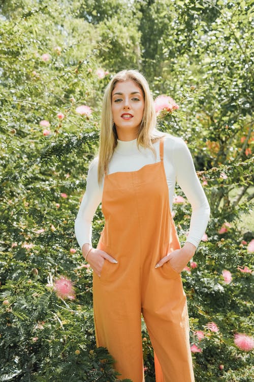 Free A woman in an orange overall jumpsuit posing in front of some flowers Stock Photo