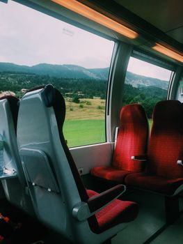 Interior of a train with red seats overlooking a scenic countryside through large windows.