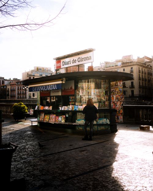 Free A bustling street kiosk in Girona, Spain, offering local newspapers and magazines under a bright, sunny sky. Stock Photo