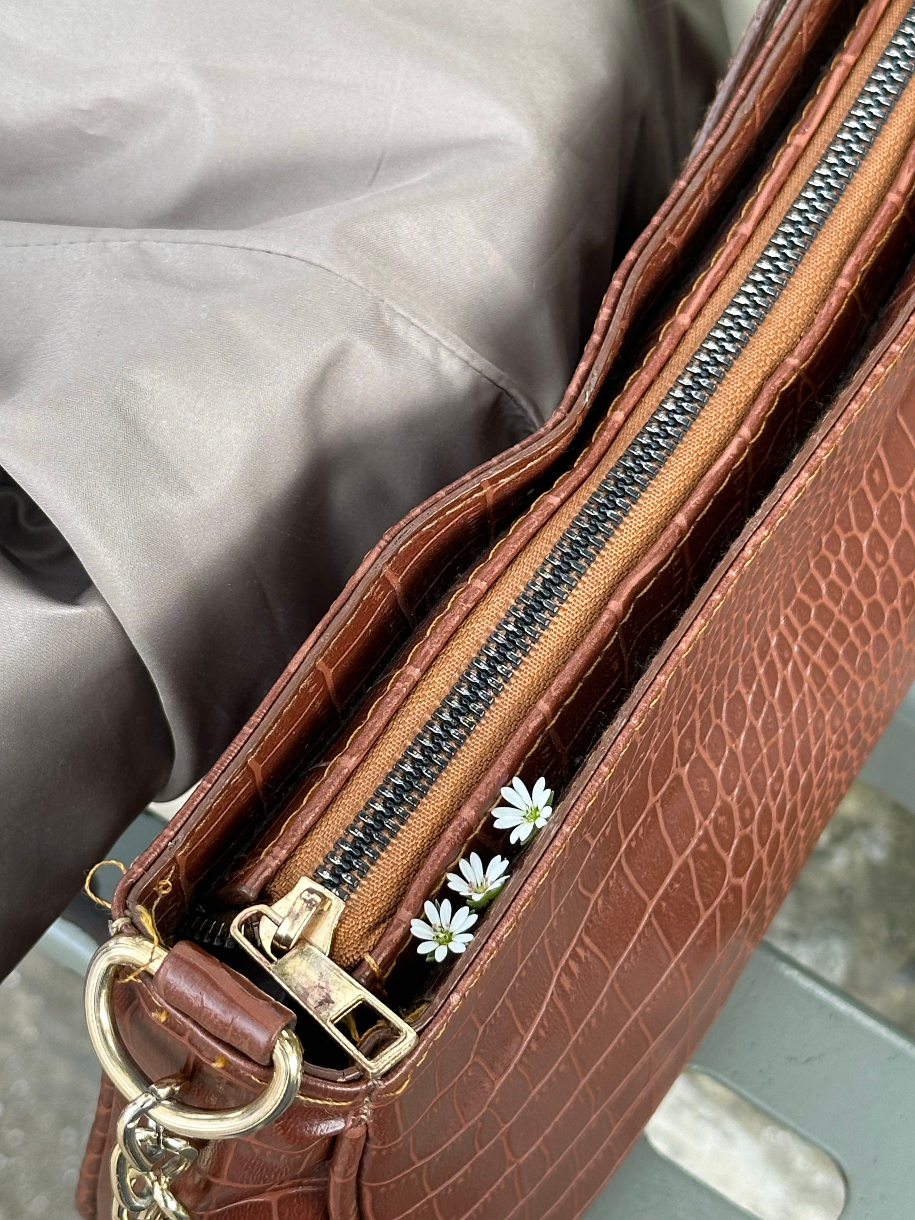 Elegant brown leather purse with delicate daisies tucked near the zipper. - handbag care tips