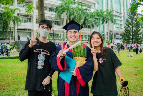 Free Three young adults celebrate graduation outdoors with joyful smiles and peace signs. Stock Photo