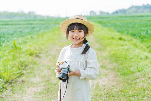 Free Joyful child in a straw hat with a camera in a lush green field on a sunny day. Stock Photo
