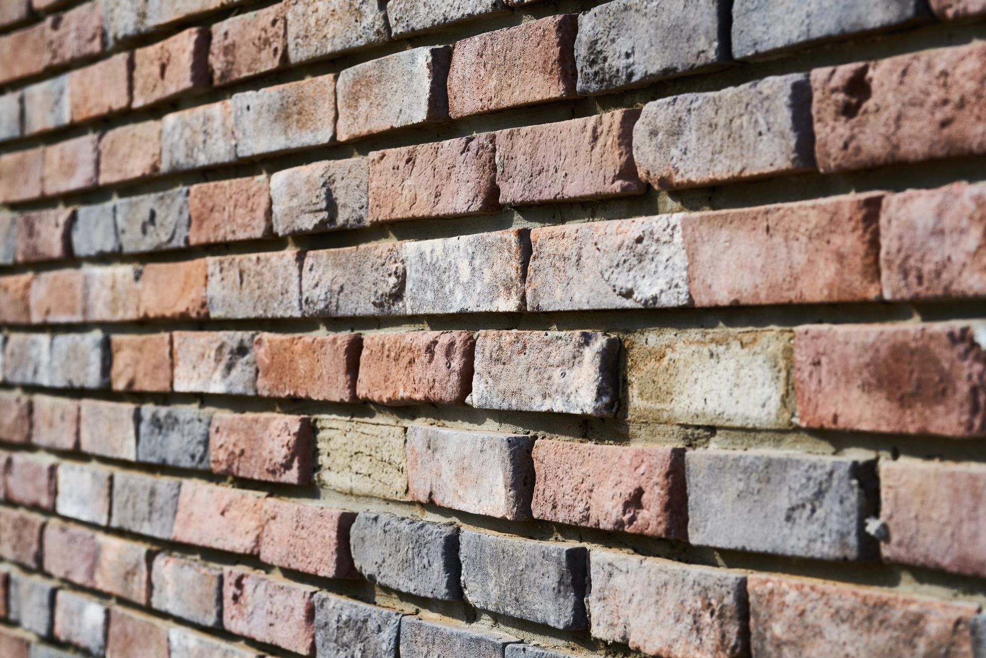 Detailed texture of a rustic red and grey brick wall with natural light shadows.