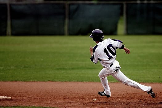 A young baseball player in uniform sprints towards base on a sunny day.