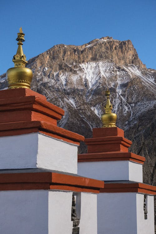 Two stupas with gold domes in front of a mountain