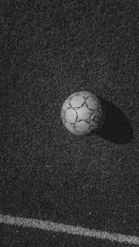 Monochrome soccer ball resting on grassy field with line marking, top view.