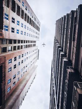 飞机在高耸的摩天大楼之间飞行，天空多云