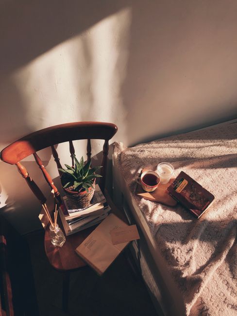 Cozy bedroom corner with a chair, books, and a cup of tea in warm sunlight.