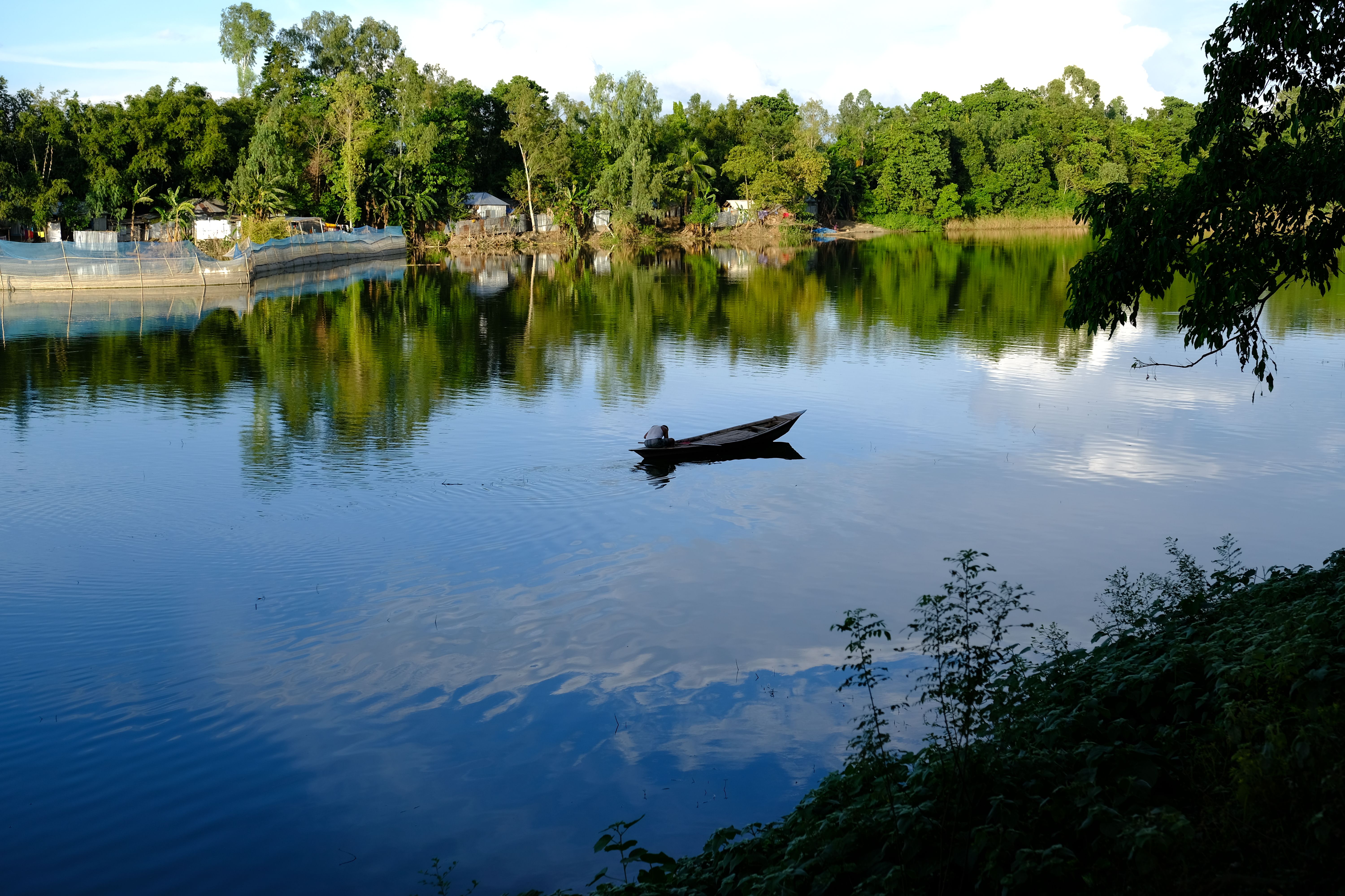 A peaceful scene of a lone boat gliding on a serene lake surrounded by lush greenery.
