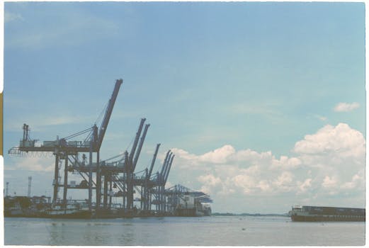 View of shipping cranes at a busy harbor against a cloudy sky.