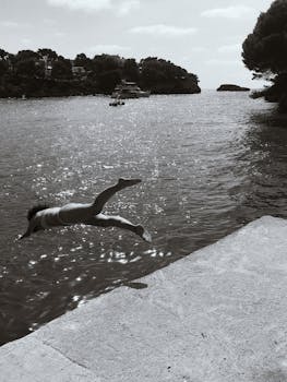 A person diving into the sparkling waters of Cala Ferrera, Spain, captured in black and white.