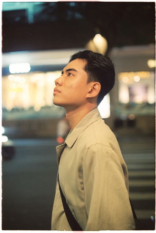 Free A young man gazing upwards on a city street at night, embodying urban style. Stock Photo
