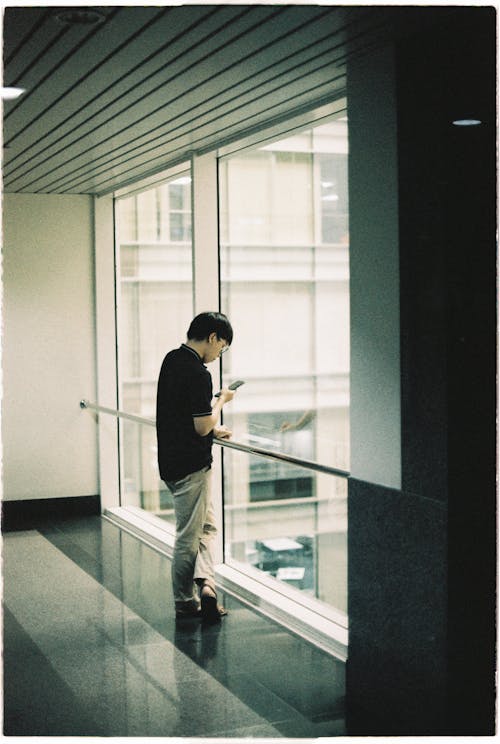 A man standing in front of a window looking at a cell phone