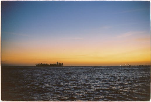 A serene view of a ship crossing the ocean horizon at sunset, capturing the warm hues of dusk.