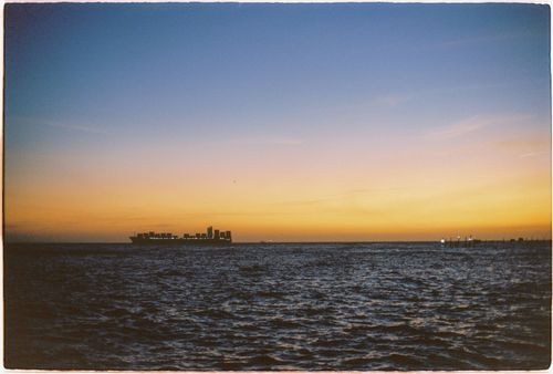 Free A serene view of a ship crossing the ocean horizon at sunset, capturing the warm hues of dusk. Stock Photo