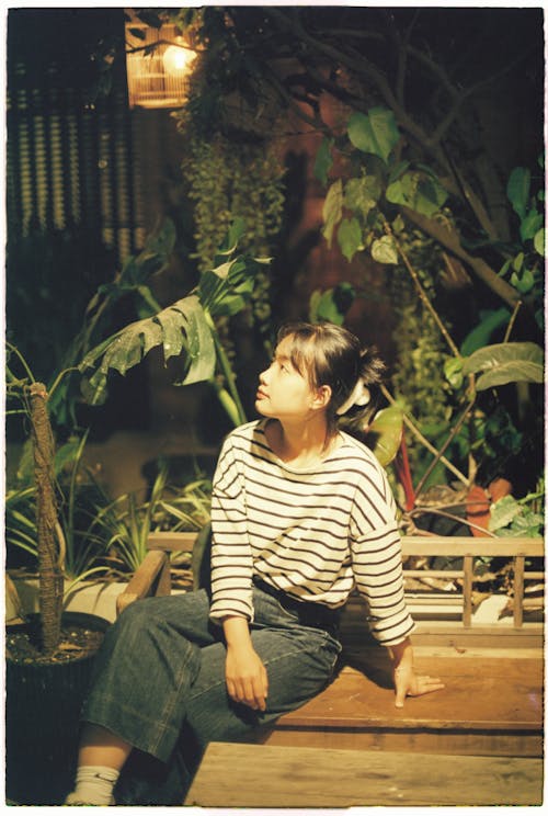 A woman sitting on a bench in front of a plant