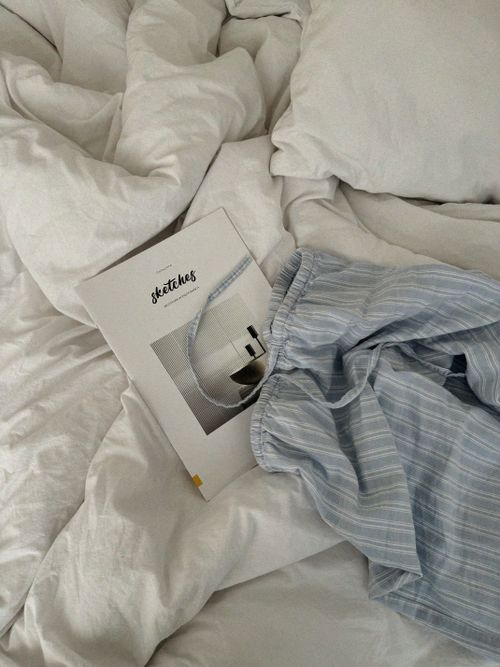 Free A cozy setup featuring a book and striped pajama pants on a white bed, evoking comfort. Stock Photo