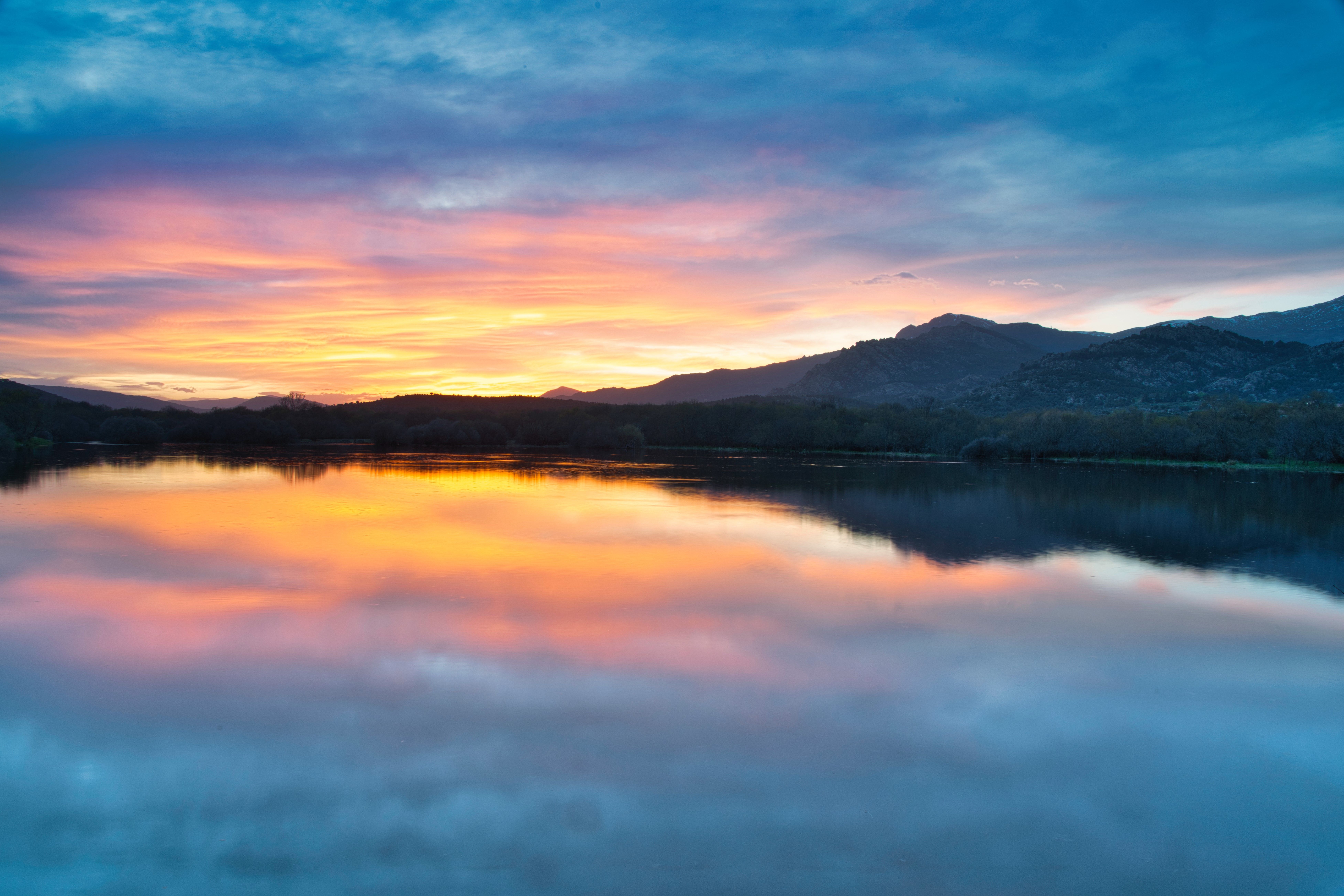 A sunset over a lake with mountains in the background · Free Stock Photo