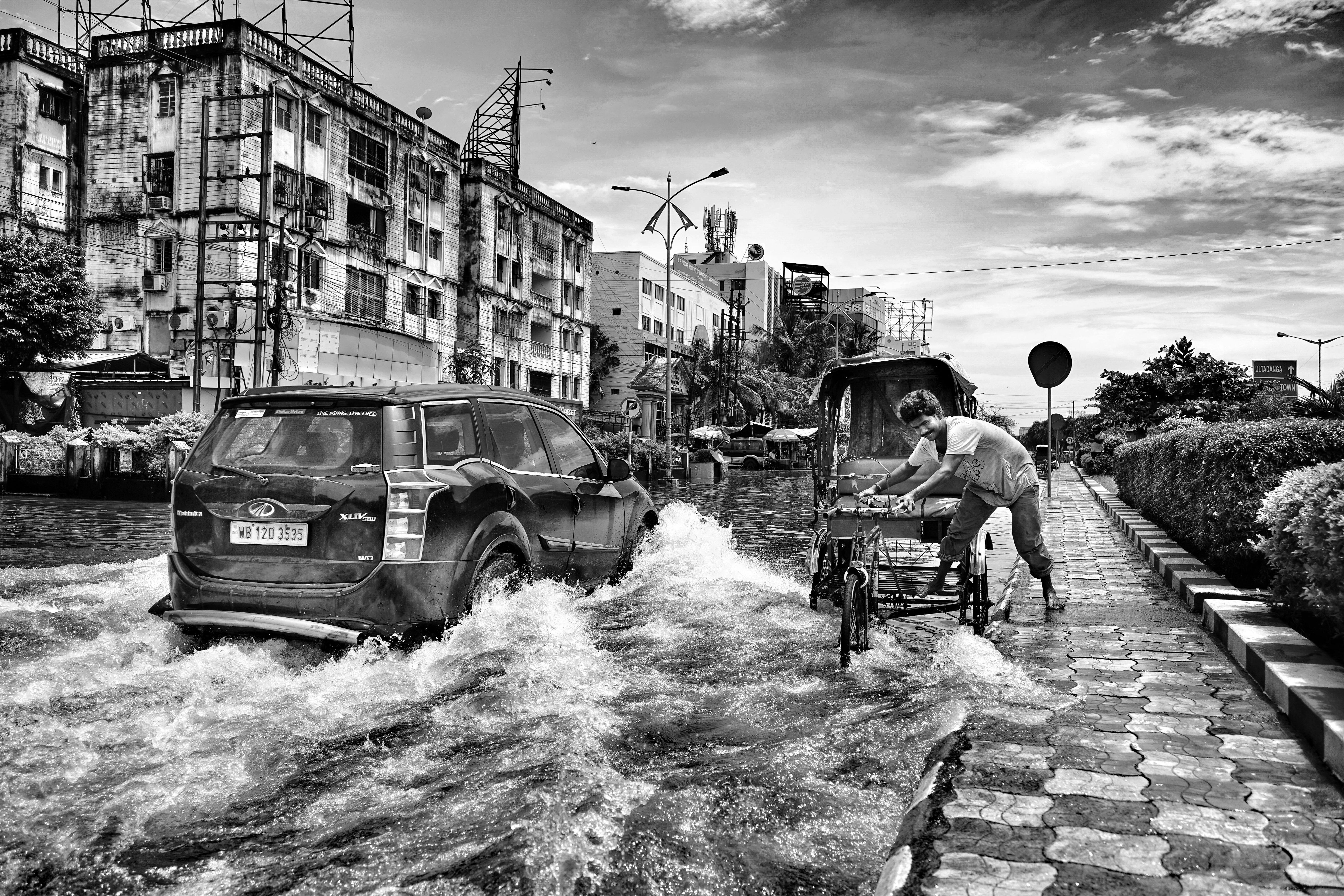Flooded street in Kolkata featuring a car and rickshaw in black and white.
