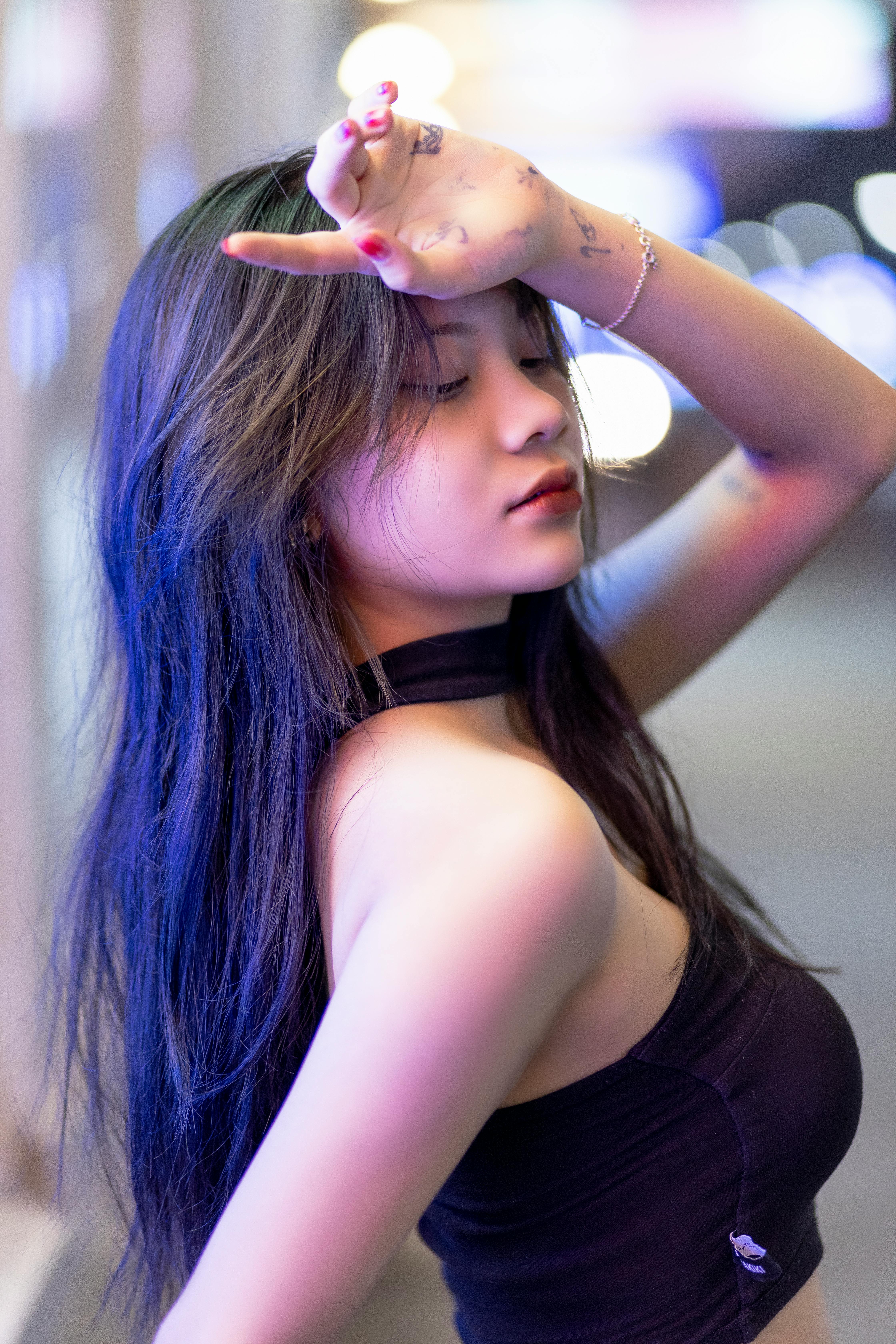 A fashionable woman poses outdoors at night, showcasing long black hair and a trendy outfit.